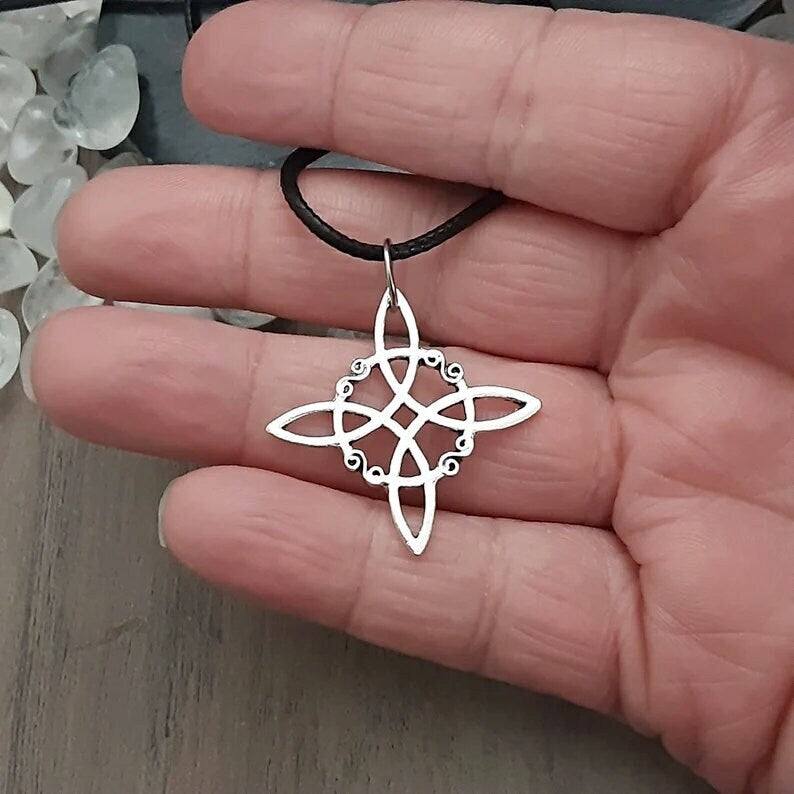 Silver Witch knot pendant charm on black cord over hand on grey wood background