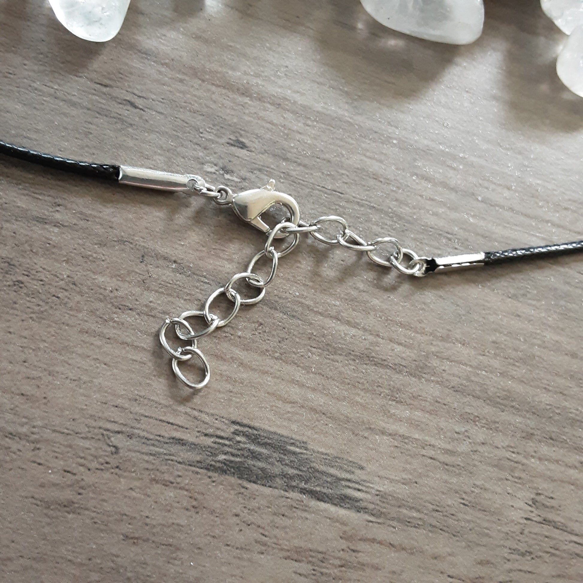 Lobster clasp and chain detailing on black cord necklace with clear Quartz tumbles and grey wooden background