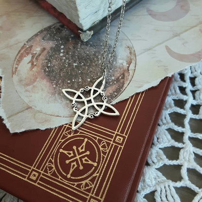 Silver color witch knot symbol pendant on silver color chainlaying on top of book/lace background