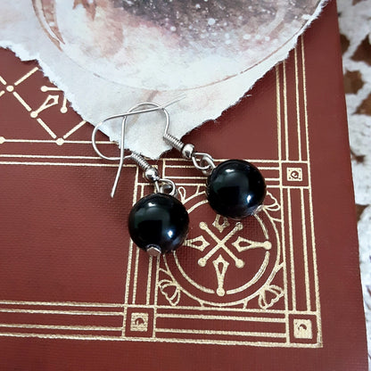 Obsidian black stone round bead earrings with silver color hooks on top of red and gold patterned book background