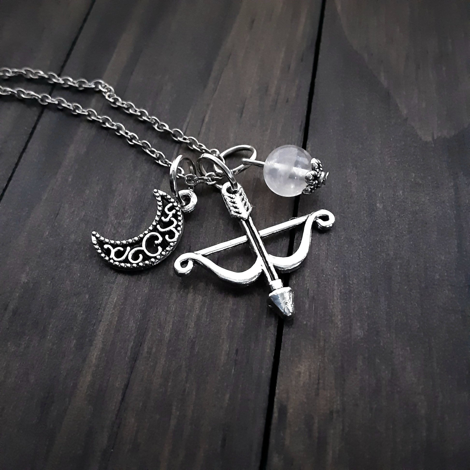 Artemis necklace for Greek Goddess of the Hunt and animals Necklace has bow and arrow charm, crescent moon charm,clear Quartz bead on silver color chain on wooden background